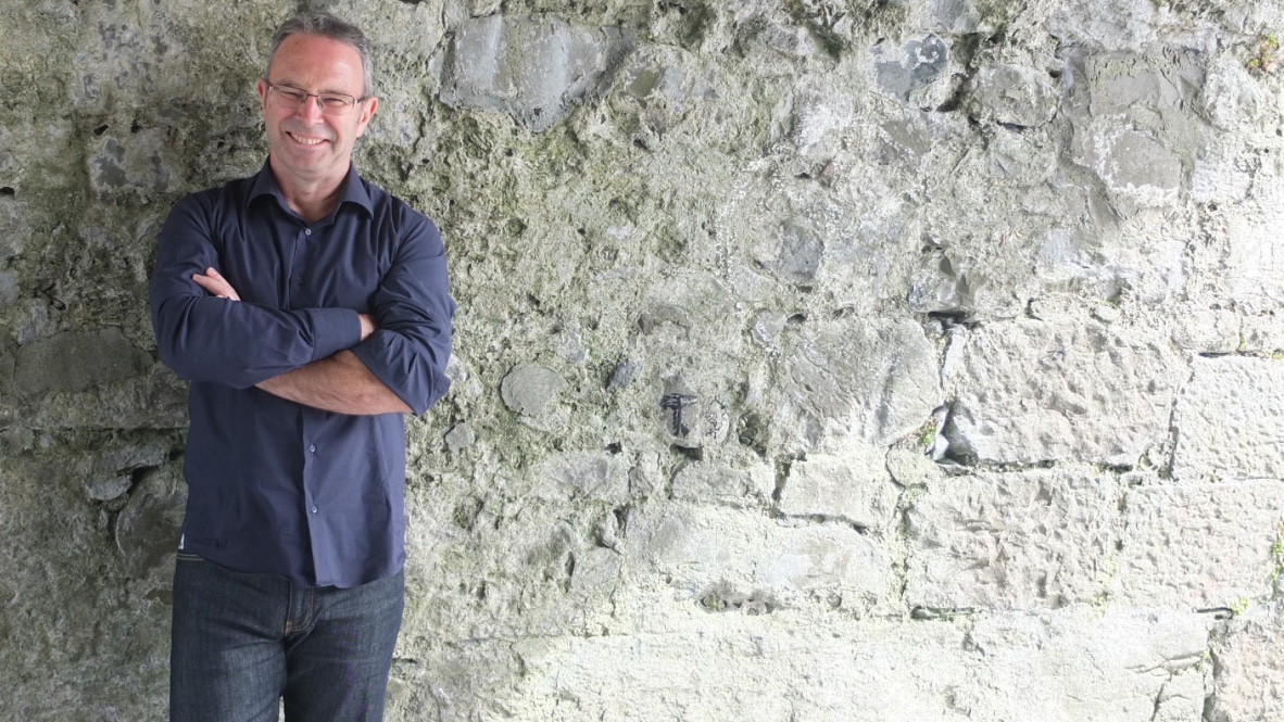 Photograph of Mike McCormack leaning against a stone wall and smiling